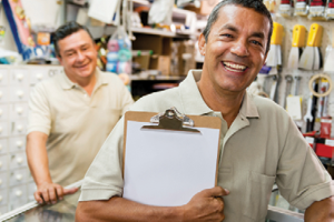 man holding clipboard in hardware store with another man in background behind a desk