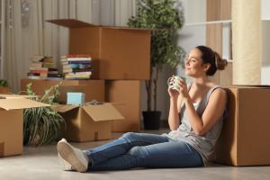 smiling woman sitting with moving boxes drinking a cup of coffee