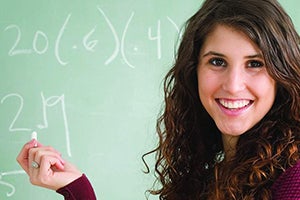 Teacher smiling holding a chalk in front of a chalk board 