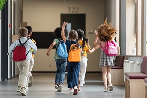 Elementary school students running through the hall of a school with their backpacks on