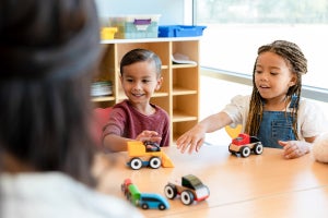 Small children sitting at a table, playing with toy cars
