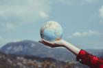 A hand holds a globe outdoors in front of a mountainous backdrop.