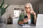 Woman at laptop looking at phone