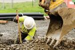 Construction worker in a hole digging dirt out with the help of a small tracked excavator