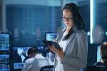 women business IT professional on tablet in surrounded by computers and other professionals