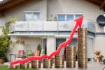 A cream colored two story house with windows is shown. There are seven stacks of coins getting incrementally larger from left to right. A red arrow is on top of the coins signifying prices going up.