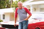 Older man in t-shirt standing in front of a red vintage car