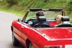 Person driving a collector car on an open road.