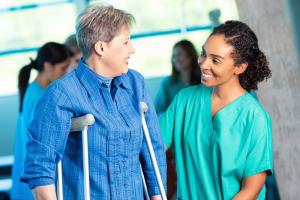 Healthcare professional safely helping woman on crutches during physical therapy session.