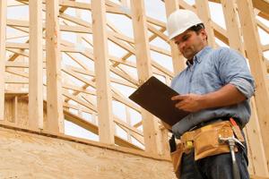 contractor with clipboard within a framed house structure