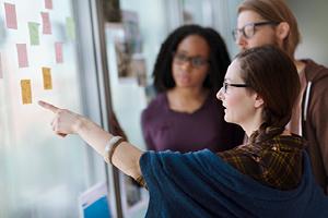 Team looking at sticky notes adhered to glass and discussing
