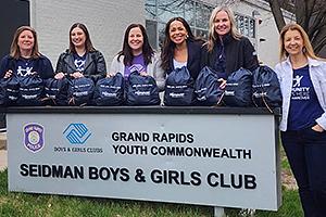 Volunteers stand behind a sign reading "Grand Rapids Youth Commonwealth, Siedman Boys & Girls Club"